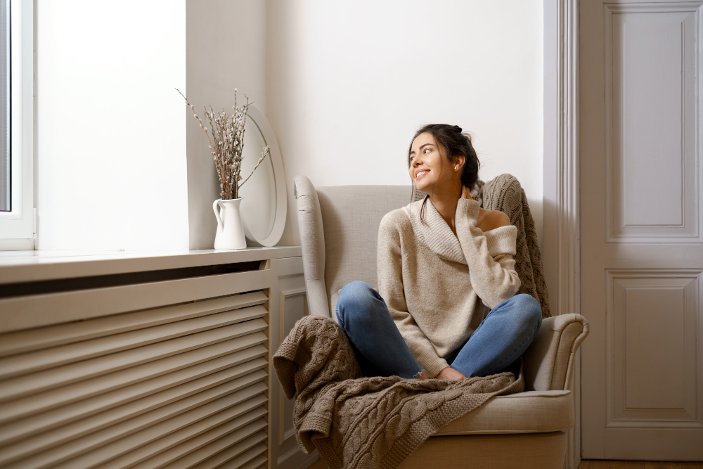 Mujer disfrutando del confort térmico en su vivienda junto a un radiador